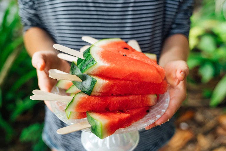 A person is holding a plate of watermelon wedges with lime seasoning. 