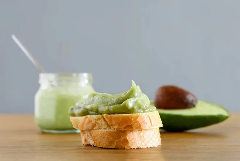 Avocado spread on toast in front of an avocado.