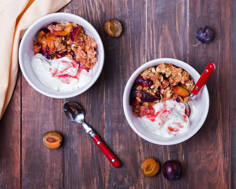 Two bowls of baked fruit with frozen yogurt on a table.