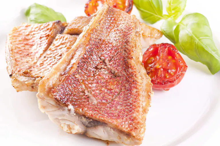 Pan-seared red snapper on plate with cherry tomato and greens