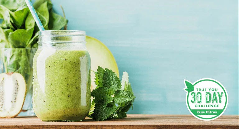 Mason jar of green smoothie beside other green fruits and vegetables