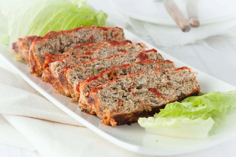 Sliced meatloaf on white plate with lettuce