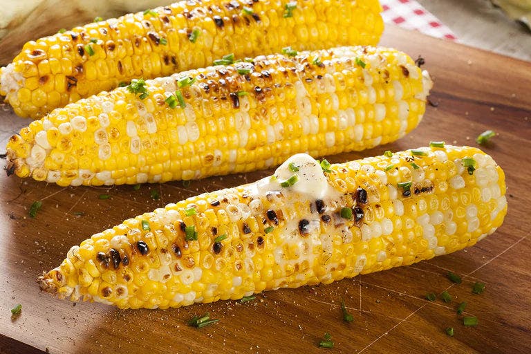 Grilled corn on cutting board garnished with chives and butter