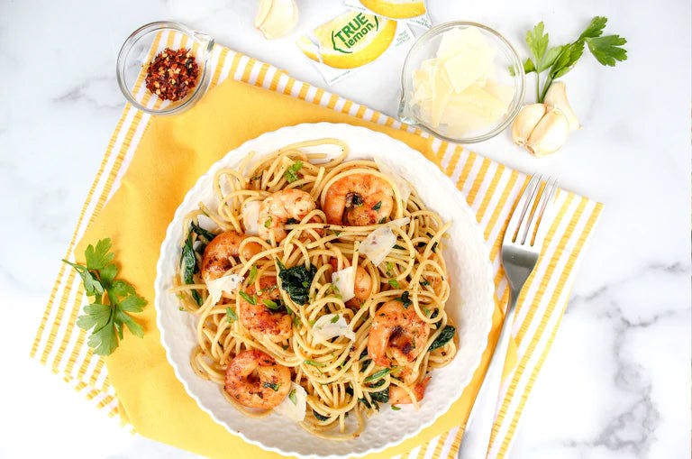 Delicious True Lemon Garlic Shrimp Pasta plated on a yellow striped table setting
