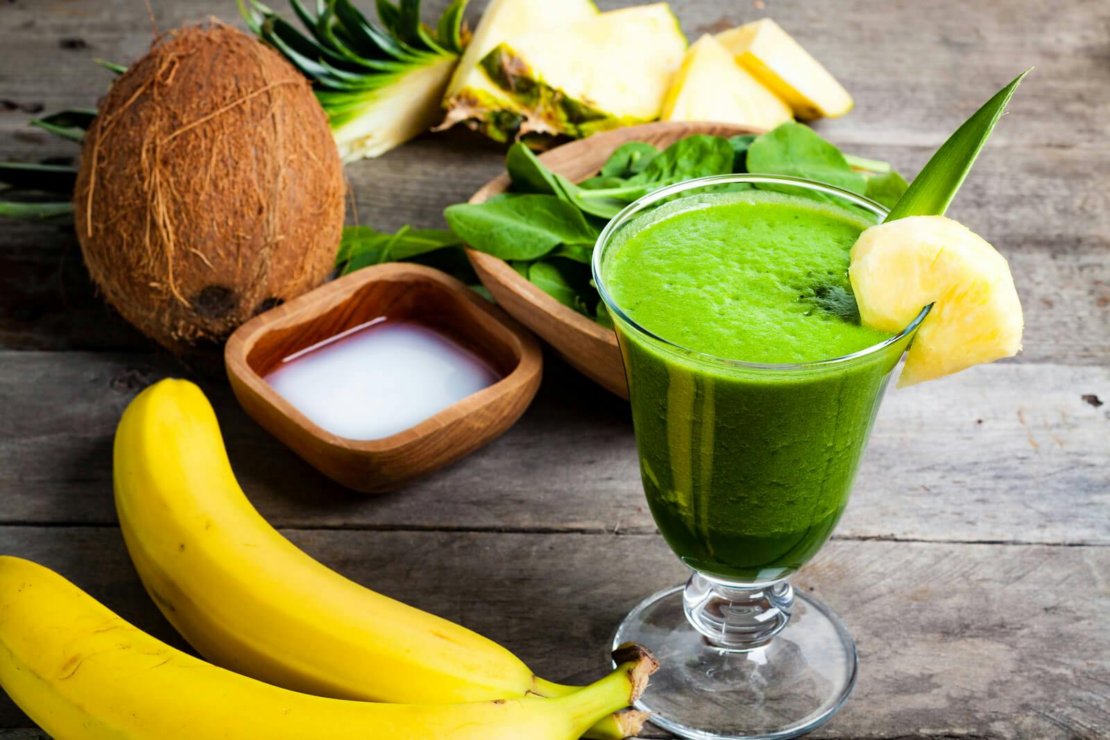 Green smoothie in glass garnished with pineapple beside various other fruits