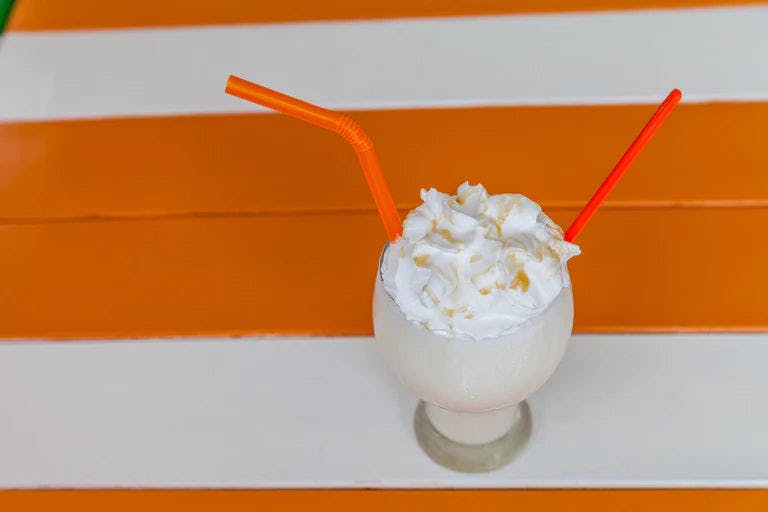 Glass of creamy beverage with whipped cream and orange straw