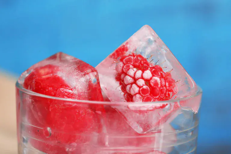 Raspberries frozen in ice cubes in glass