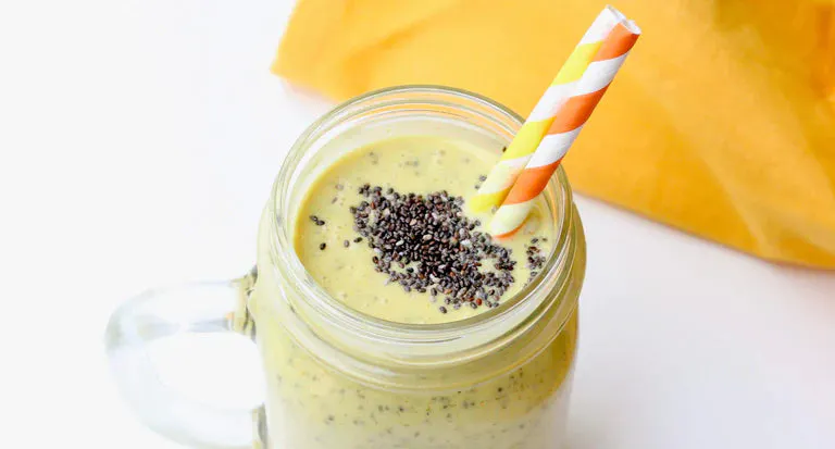 Yellow smoothie in glass jar with chia seeds on top and two straws