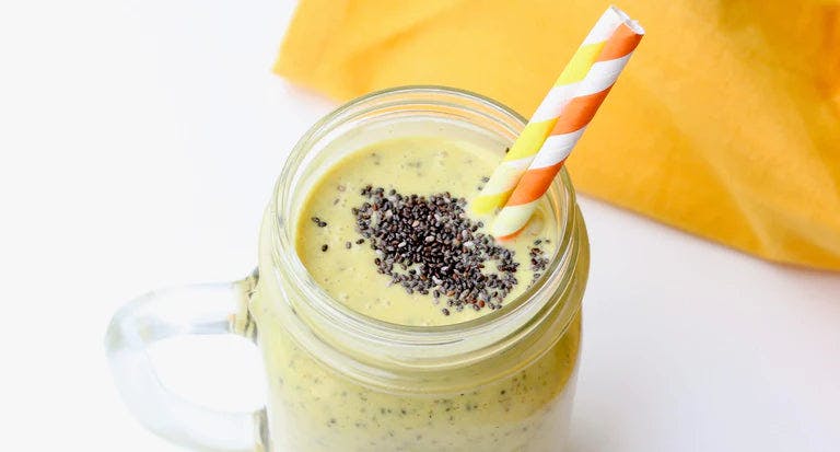 Yellow smoothie in glass jar with chia seeds on top and two straws