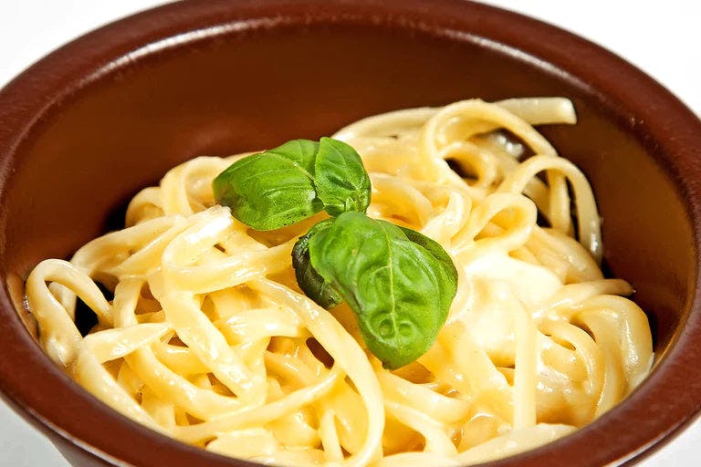 Creamy linguine in brown bowl with basil garnish