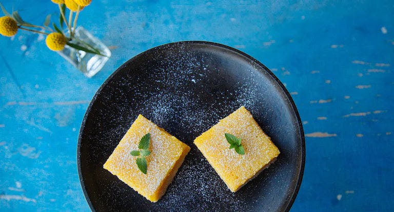 A plate of delicious lemon bars garnished with mint on a dish.