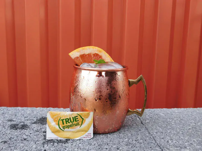 Copper cocktail glass filled with a spritz, True Grapefruit packet in front.