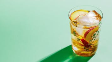 Peach Green Tea Punch in a glass on a green background.