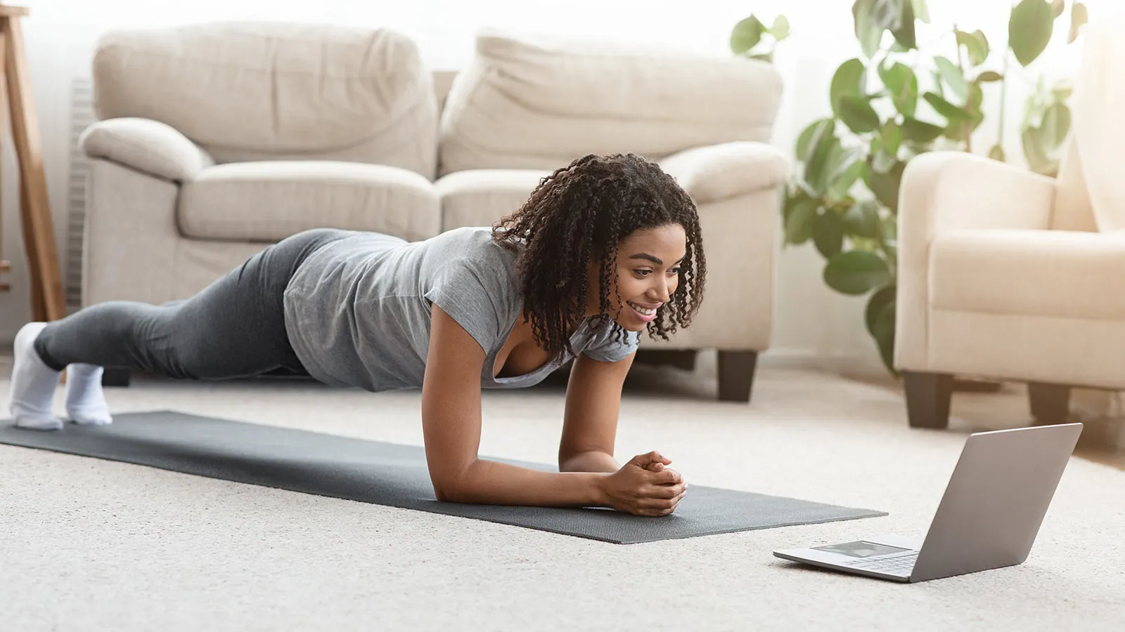 Woman doing a plank in living room in front of a laptop