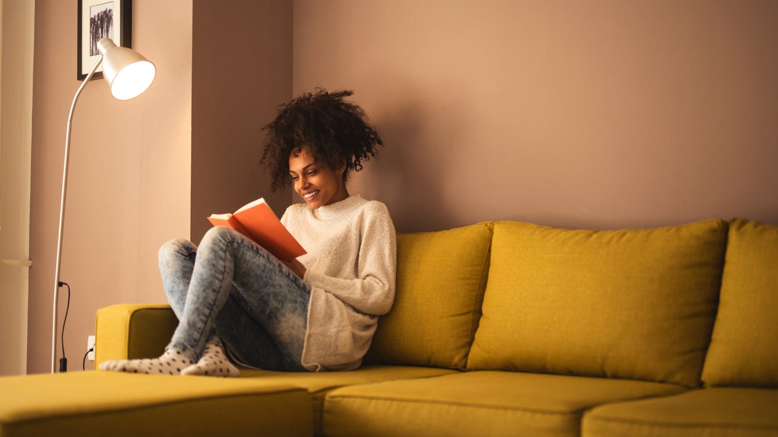 A woman sits on a couch and is reading a book.