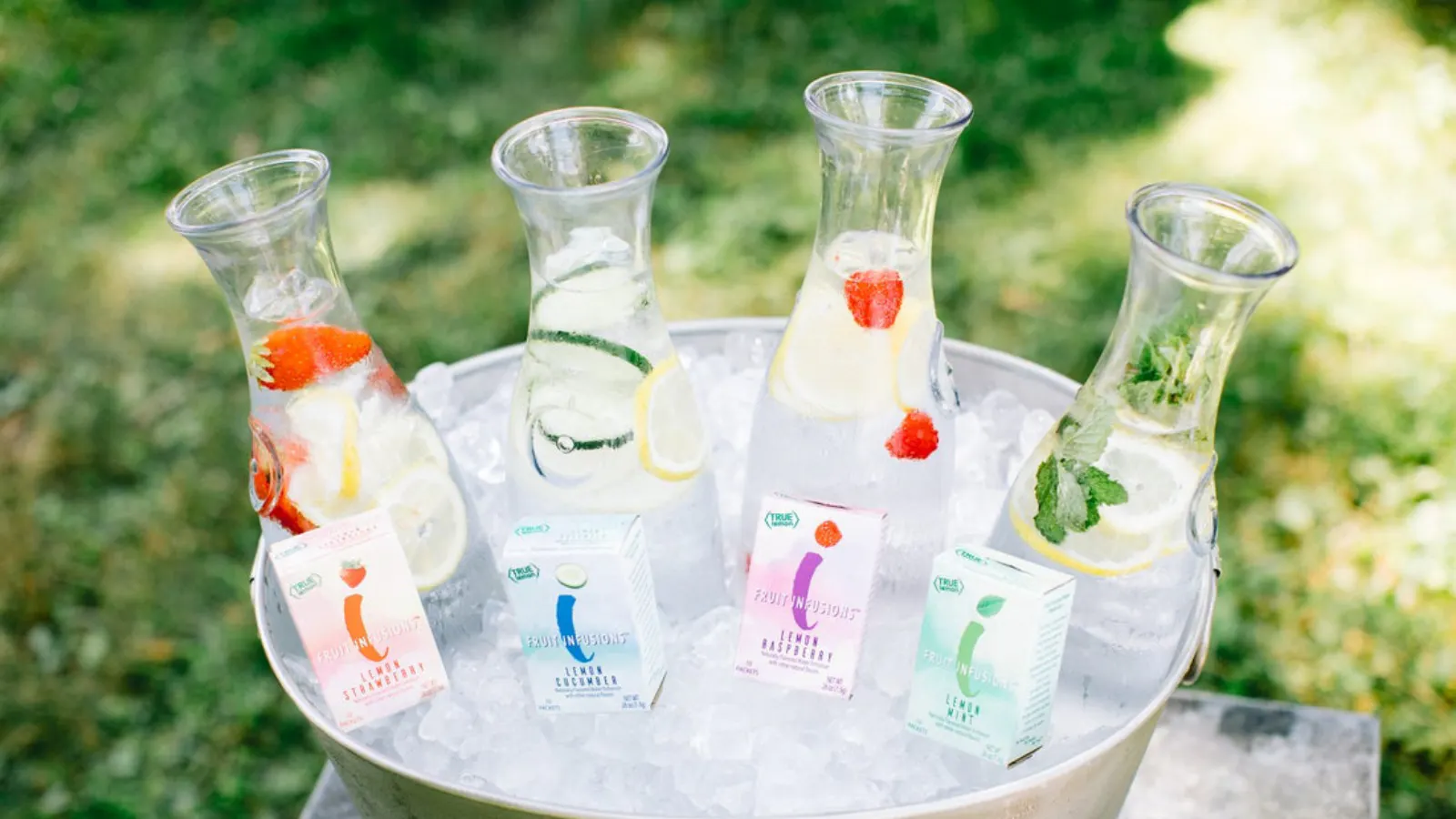 A tub of ice with glass pitchers filled with Fruit Infused water. Boxes of True Lemon Fruit Infusions sit in the ice in front of the pitchers.