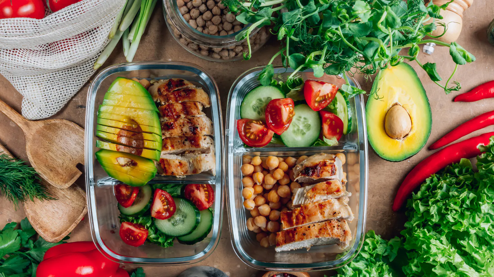 Two tupperware containers of healty foods on a table surrounded by ingredients.