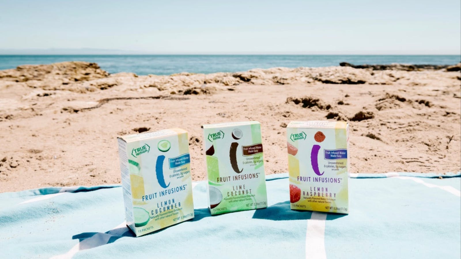 Three boxes of True Lemon Fruit Infusions on a blanket at the beach.