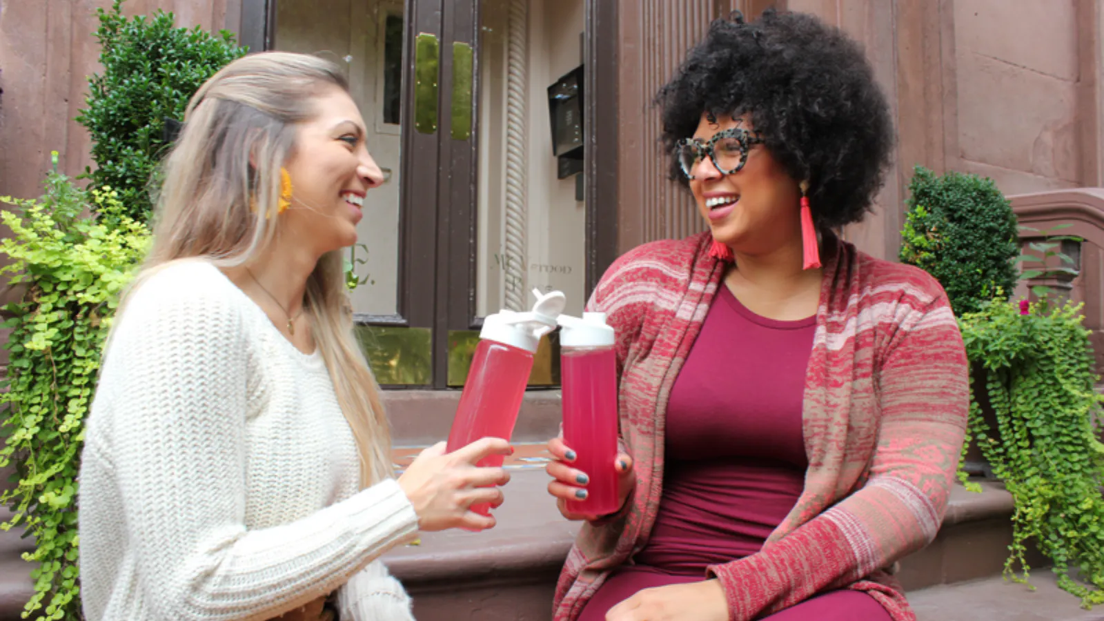Two woman sit across from each other on some stairs. They are laughing.