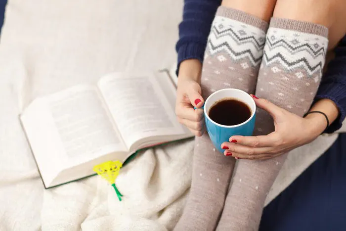 women in tall socks drinks coffee while reading a book