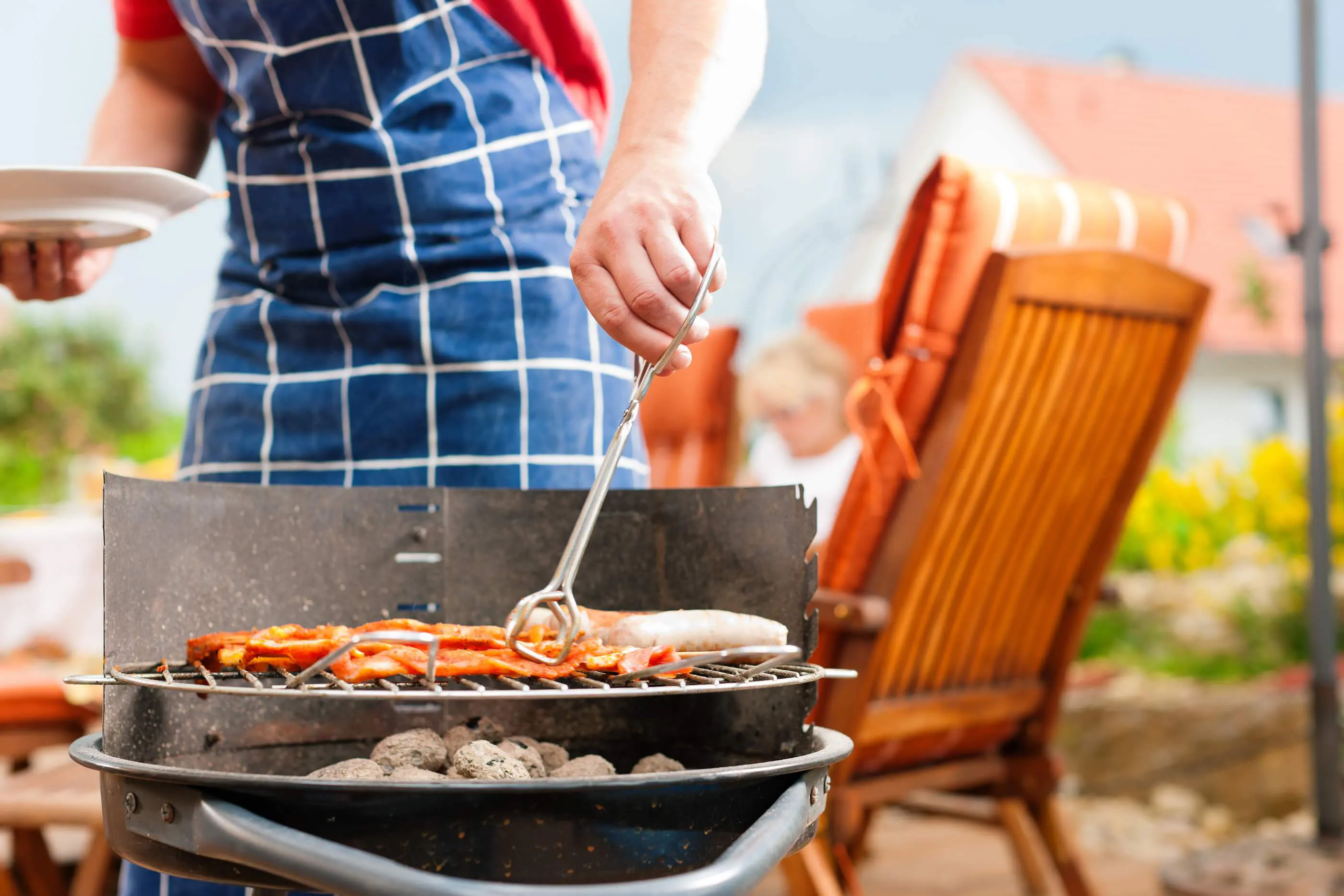 man cooks chicken over a charcoal grill on a summer day