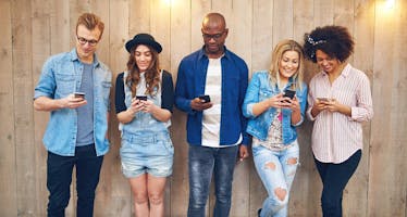 friends check their phones together against a wooden wall