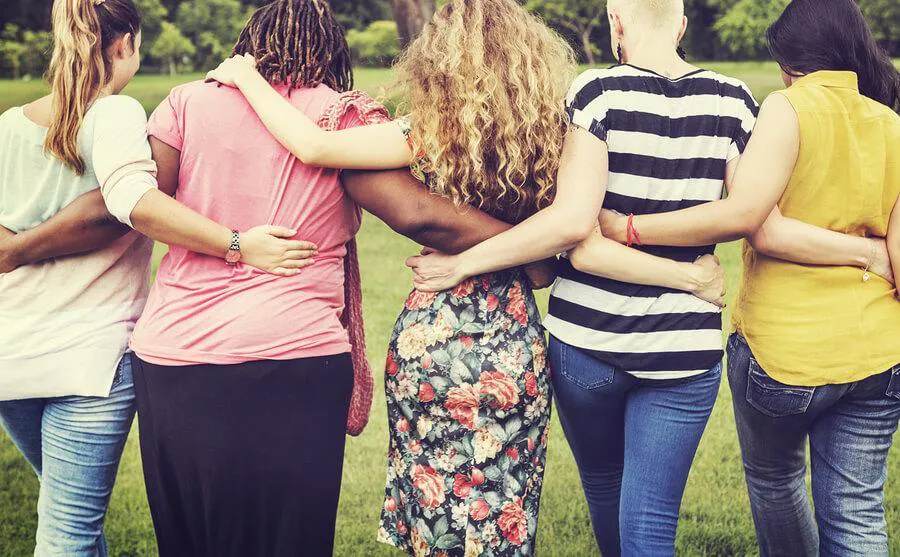 Five women embracing while walking away from camera.