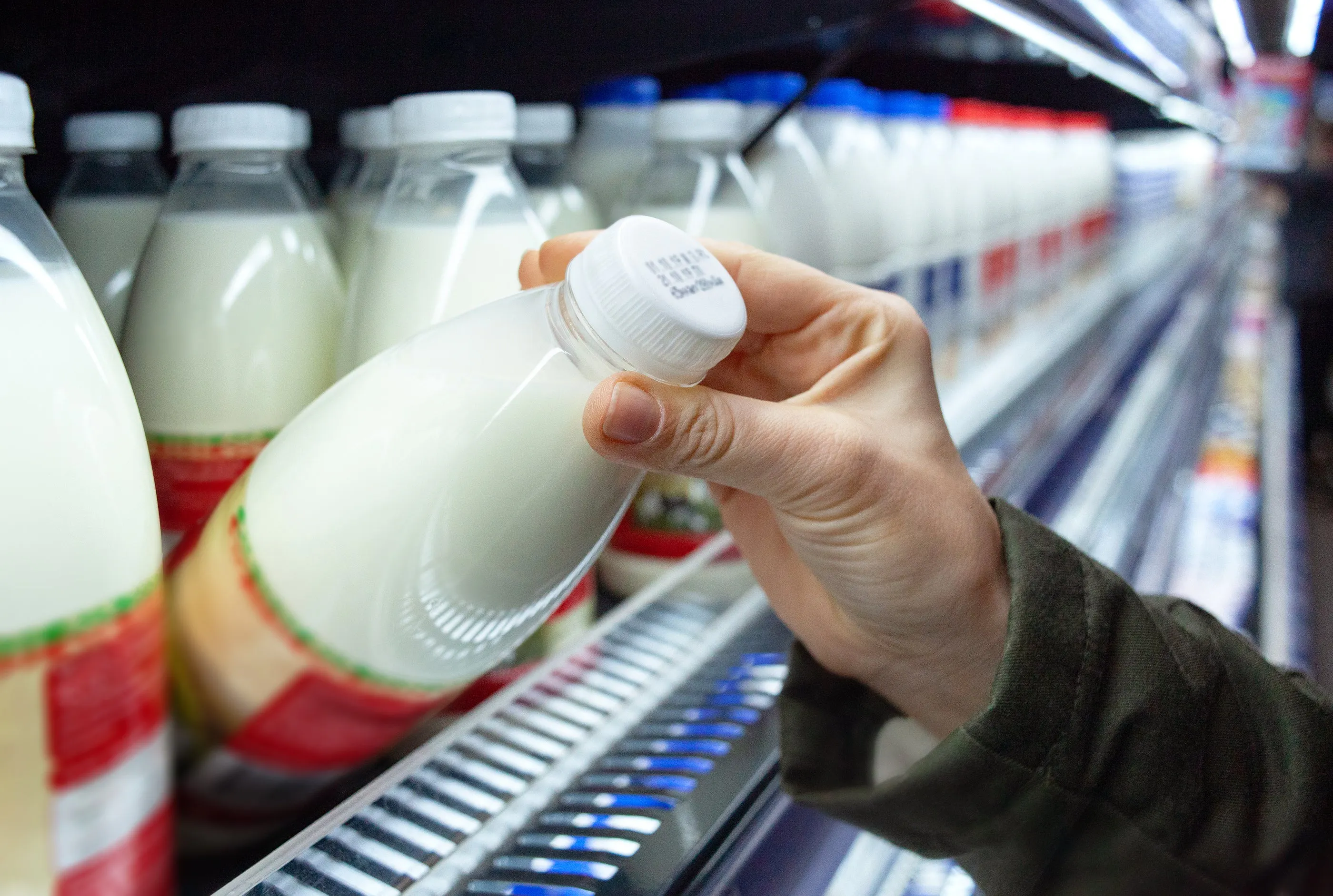 hand grabbing plastic bottle of milk off of refrigerator shelf
