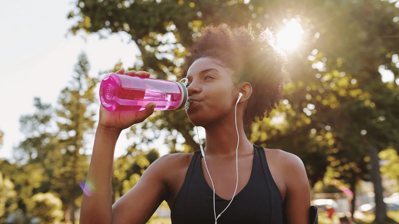 Woman wearing earbuds is walking outside and drinking a True Lemon drink out of a water bottle.