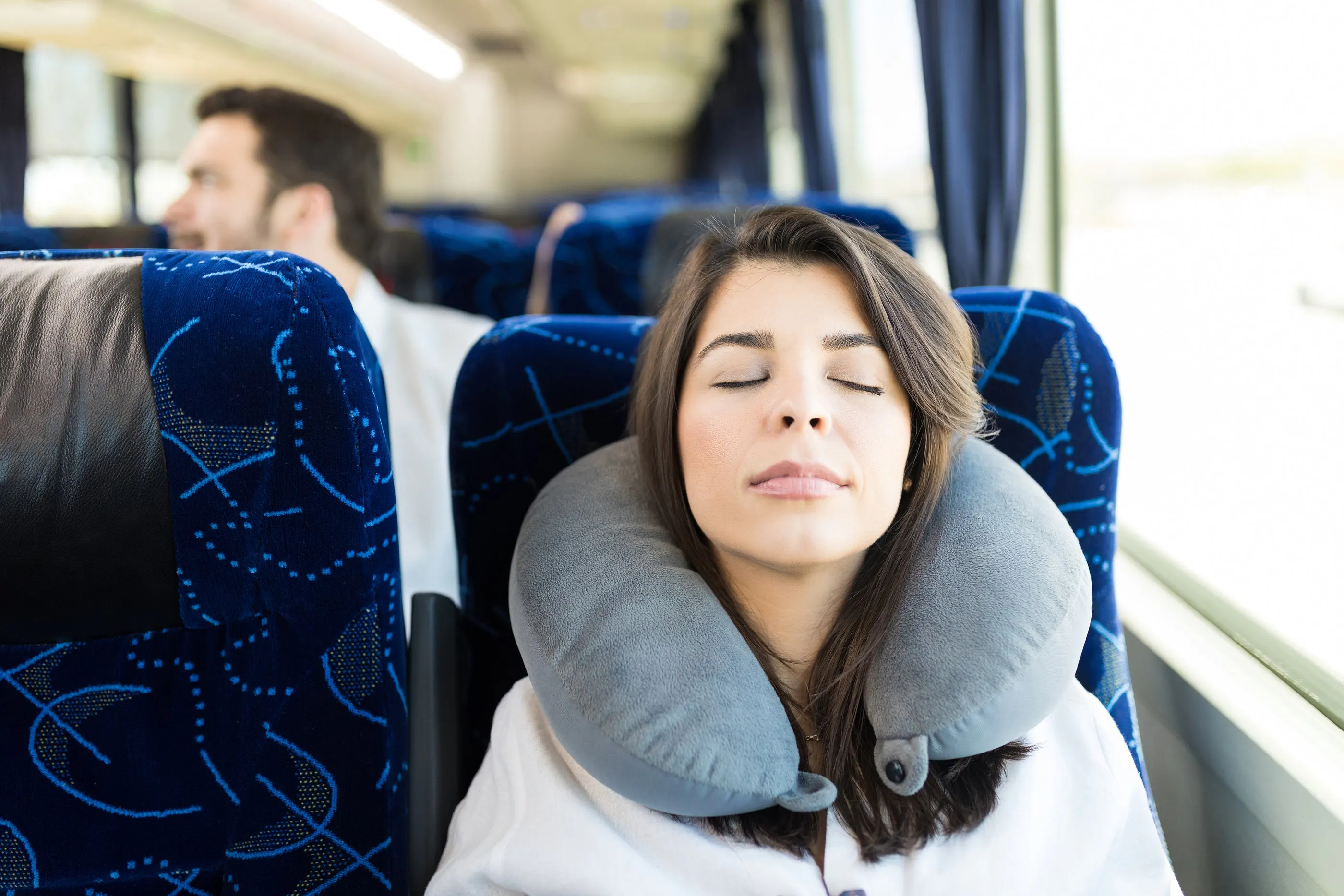 woman with shut eyes with grey neck pillow around neck