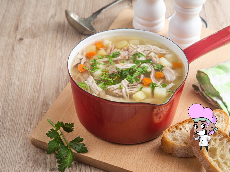 Red pot of chicken soup with carrots and potatoes garnished with herbs