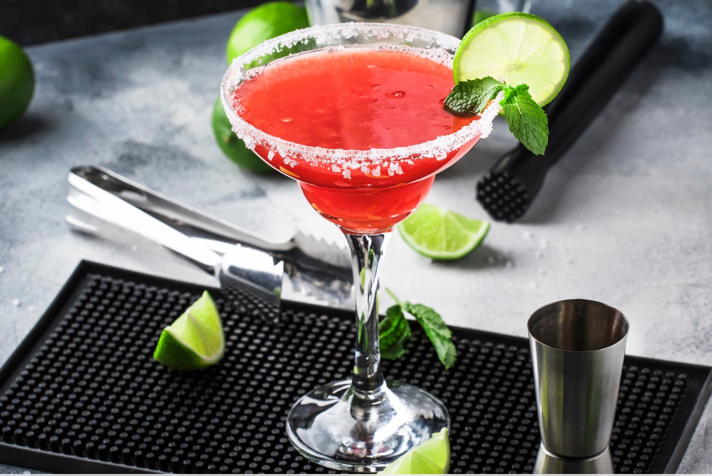 Watermelon margarita in a glass with a salted rim and tongs and bar tools in the background.