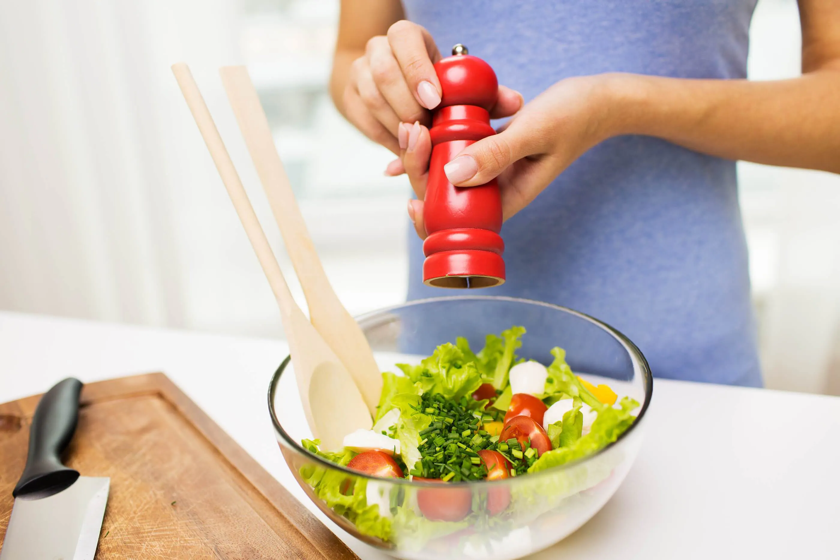 a woman puts salt on a fresh salad with salt grinder