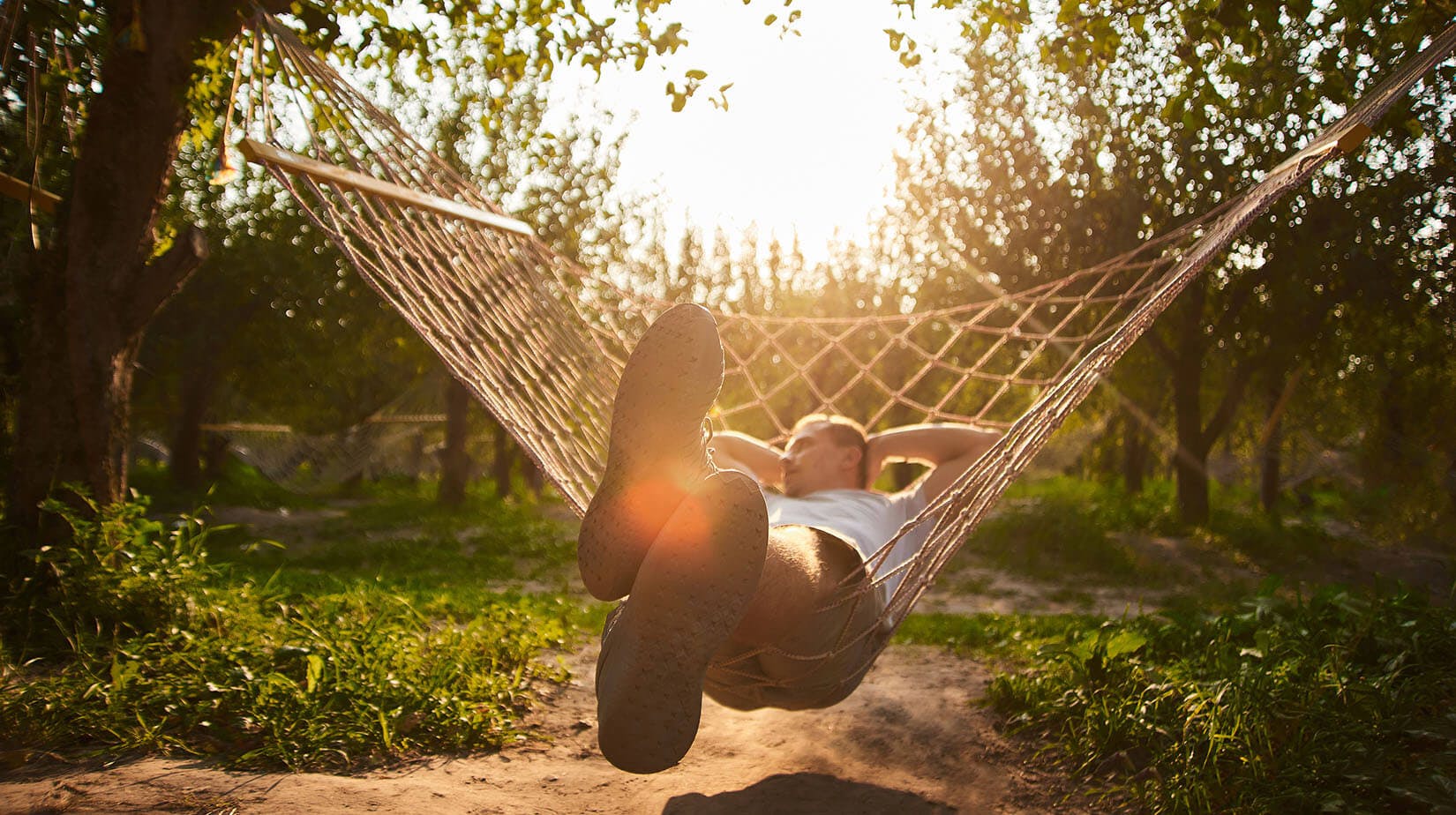 man laying in hammock in the woods with sun in background