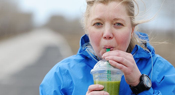 Woman outside in blue jacket drinks green smoothie