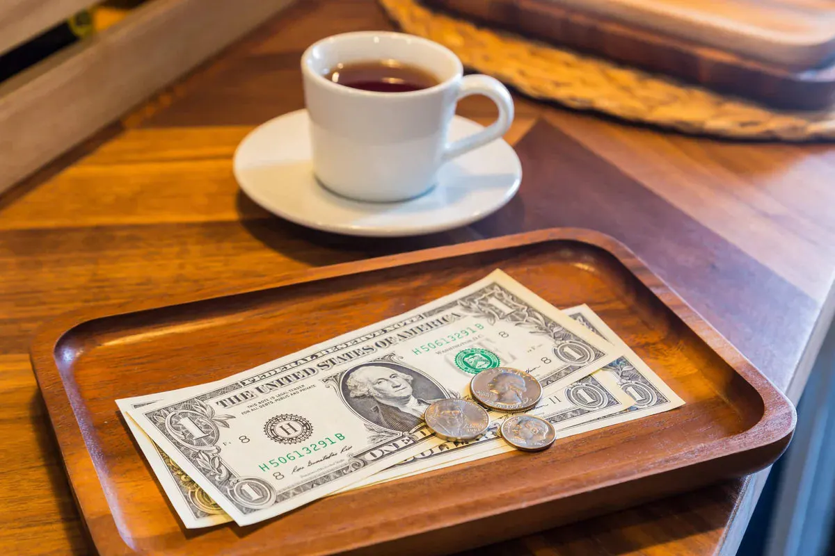 bills and coins on wooden tray with coffee in background