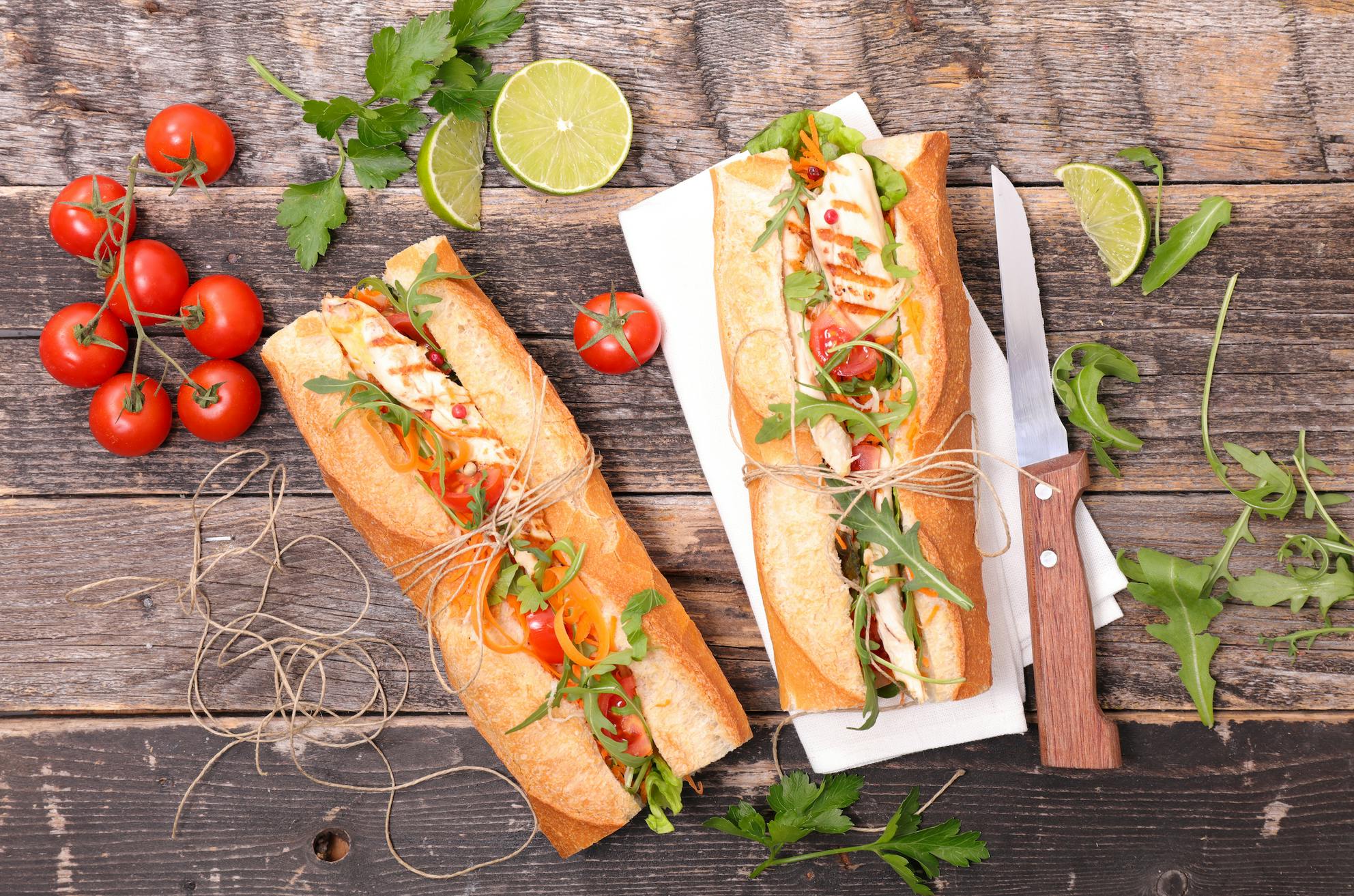 Bright bahn mi like sandwich spread with garnishes of herbs, lime, and tomato