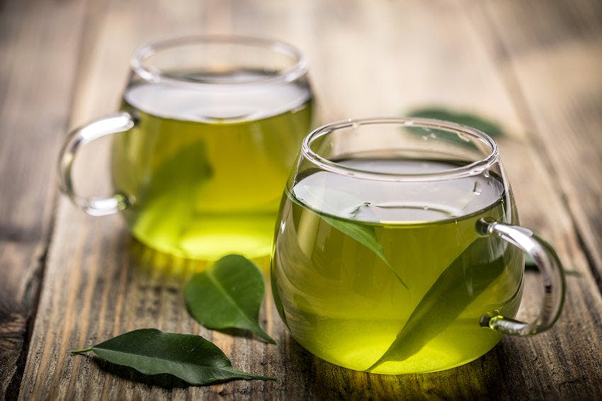 Two cups of green tea in glass cups on a wooden table.